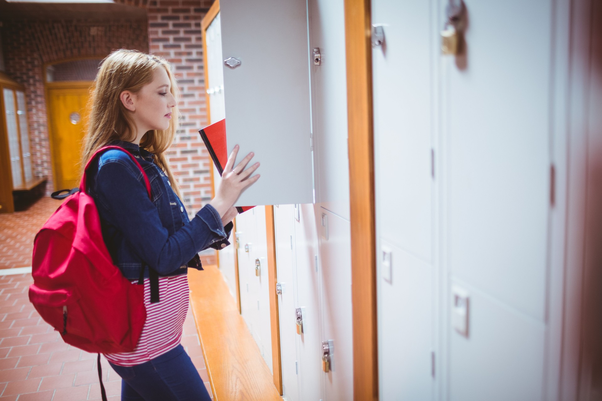 Pretty student with backpack putting notebook in the locker